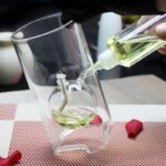 A person pouring a yellow liquid into a glass with a unique, curved design, demonstrating a science experiment or demonstration.