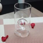 Transparent glass cylinder containing a detailed brain model, surrounded by small red bone-shaped objects on a textured surface.