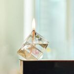 A close-up of a glass cube candle with a burning wick, showcasing the melting wax and delicate flame.