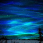 Aurora borealis illuminating the night sky with vibrant green and blue hues over a snowy landscape.