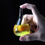 Hand holding a glass chemical flask filled with yellow liquid, showcasing a science experiment.
