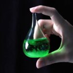 Green liquid in a laboratory flask held by a hand.