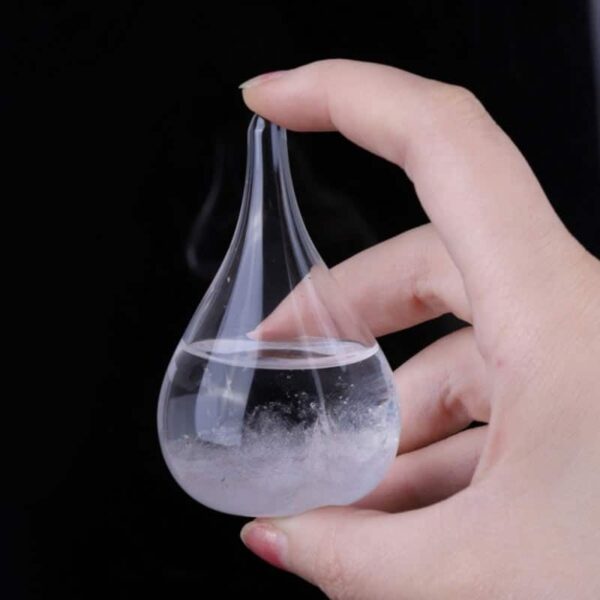 Close-up of a glass Erlenmeyer flask containing liquid and vapor, held by a hand against a black background, demonstrating a science experiment or chemical reaction.