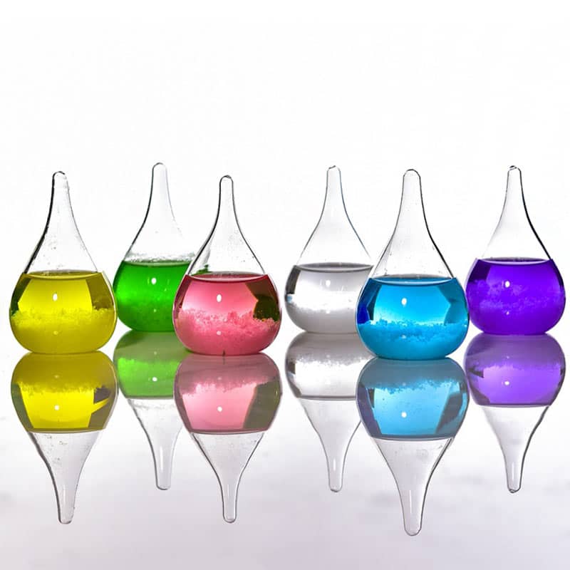 Colorful laboratory glassware with liquids in yellow, green, pink, clear, blue, and purple, reflecting on a smooth surface.