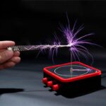 Hand holding a spark generator creating purple electrical sparks over a black surface, demonstrating static electricity for educational science experiments.