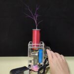 Small Tesla coil producing visible lightning sparks with a hand adjusting the device, demonstrating high-voltage electrical phenomena for educational purposes.