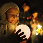 A young girl holding a glowing moon lamp, exploring its light in a dark setting.