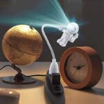 Earth globe with astronaut lamp projecting light, placed next to a wooden clock on a desk.