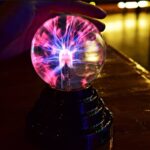 A person touching a plasma globe with visible colorful electrical discharges inside, showcasing a Tesla coil effect.