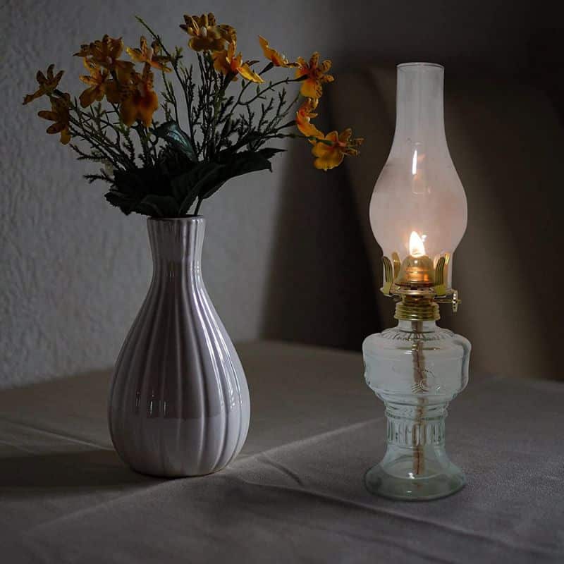 Vintage oil lamp and ceramic vase with yellow flowers on table, creating a cozy, nostalgic atmosphere in a softly lit room.