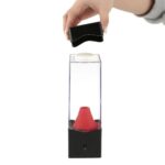 Hand placing black lid on a science experiment device with a red cone inside a transparent container.