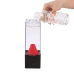 Hand pouring water into a transparent water rocket launcher with a red nozzle, set against a white background.