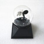 Small Tesla coil model inside a glass bulb on a black base, demonstrating electromagnetic principles.