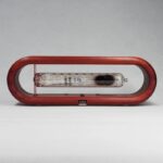 Glass tube with black substance inside, mounted within a red wooden frame, showcasing a scientific experiment or demonstration.