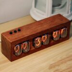 Vintage nixie tube clock displaying time on a wooden base, with a modern electronic device in the background.