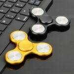 Two fidget spinners, one black and one gold, resting on a computer keyboard, showcasing popular stress-relief toys with metallic accents.