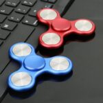Colorful fidget spinners, red and blue, resting on a black keyboard, ideal for stress relief and focus enhancement.