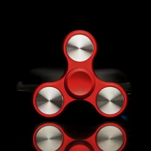 Red fidget spinner with metallic circular weights on a black background, designed for stress relief and focus enhancement.