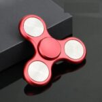 Red fidget spinner with three spinning arms, designed for stress relief and focus enhancement, placed on a dark surface.