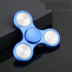 Blue fidget spinner with metallic accents, designed for stress relief and focus enhancement, placed on a reflective black surface.