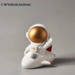 A cute astronaut figurine with a gold helmet, sitting on a white rocket-shaped base, perfect for science-themed decor or educational purposes.