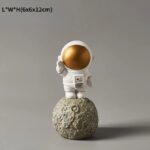 Small astronaut figurine with a gold helmet standing on a textured moon rock, ideal for science-themed decor or educational displays.