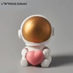 Adorable astronaut figurine holding a pink heart, featuring a shiny gold helmet and white suit, perfect for science-themed decor or educational toys.