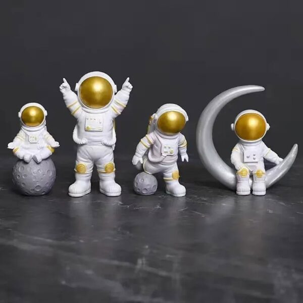 Set of four astronaut figurines with gold helmets, one sitting on a moon-shaped object, one standing on a textured planet, and two sitting on a crescent moon, all against a dark background.