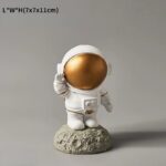 An adorable astronaut figurine with a gold reflective helmet, standing on a moon-like surface, perfect for science decor and educational displays.