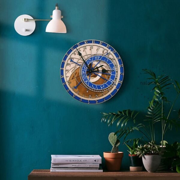 Decorative wall clock featuring zodiac signs and intricate design, mounted on a teal wall with modern white wall lamp, complemented by potted plants and a stack of magazines on a wooden surface.