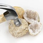 Close-up of a hammer breaking a geode rock to reveal sparkling crystals inside, showcasing geological and educational science tools.
