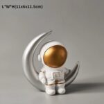 Cute astronaut figurine with a golden helmet, standing on a silver crescent moon. Perfect for science-themed decor and educational purposes.