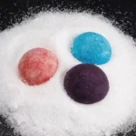 Vibrant blue, pink, and purple bath bombs resting on white powder, showcasing colorful, spherical bath products for relaxation and skincare.