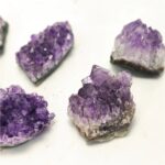 Four vibrant purple amethyst crystal clusters on a white background, showcasing their natural crystalline structure and deep violet color, ideal for educational displays or home decor.