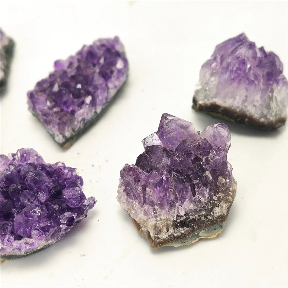 Four vibrant purple amethyst crystal clusters on a white background, showcasing their natural crystalline structure and deep violet color, ideal for educational displays or home decor.