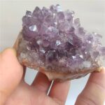 Close-up of a purple amethyst crystal geode held between fingers, showcasing vibrant crystalline structures and natural beauty.