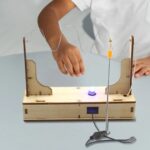 Child conducting a magnetic field experiment with a DIY science kit, featuring wires, a magnet, and a wooden frame for educational science activities.