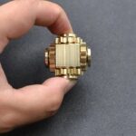 Small gold gear model held between fingers, showcasing intricate mechanical design for educational and decorative purposes.