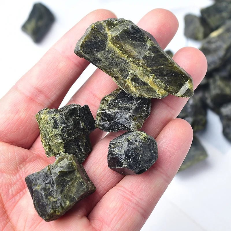 A close-up of a hand holding several greenish-black mineral crystals with a rough texture and shiny surfaces.