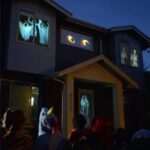 Haunted house decorated with glowing ghost and skeleton window displays, creating a spooky atmosphere for Halloween night.