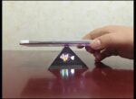 Innovative smartphone hologram projector displaying a 3D fish model on a pyramid stand.
