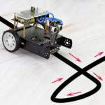 Small robotic car following a black line on a white surface, equipped with sensors and wheels, demonstrating line-following technology for educational purposes.