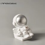 A cute astronaut figurine with a silver helmet, sitting on a white base, perfect for science-themed decor or educational displays.