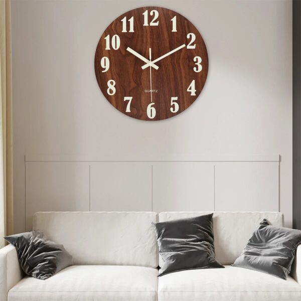 Elegant round wooden wall clock with white numerals and hands, mounted above a white sofa with black cushions in a contemporary living room setting.