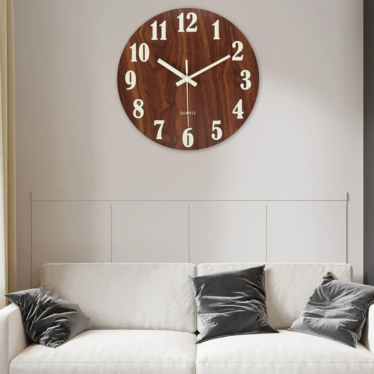 Modern Wooden Wall Clock in Living Room Elegant round wooden wall clock with white numerals and hands, mounted above a white sofa with black cushions in a contemporary living room setting.