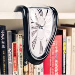 A melting clock sculpture inspired by Salvador Dalí's surrealist art, draped over a row of books on a shelf. The clock appears to be melting and distorted, creating a dreamlike and artistic visual.