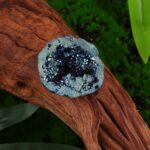 Close-up of a blue and silver geode resting on a wooden surface, showcasing sparkling crystals and intricate textures.