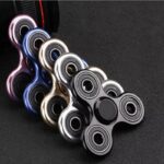 Colorful fidget spinners in various metallic finishes arranged on a dark surface, showcasing their smooth design and spinning capability.