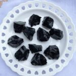 Collection of black obsidian crystal rocks displayed on a white decorative plate, ideal for science decor and educational purposes.
