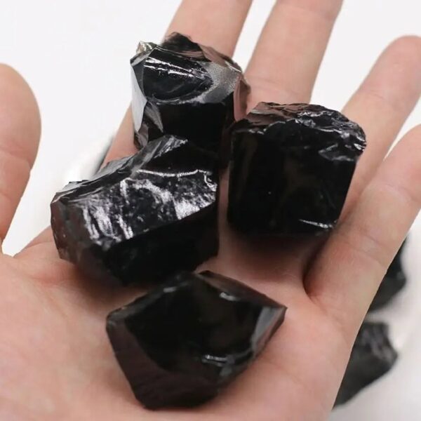 Close-up of shiny black obsidian rocks held in a person's hand, showcasing their smooth, glassy surface and natural irregular shapes.